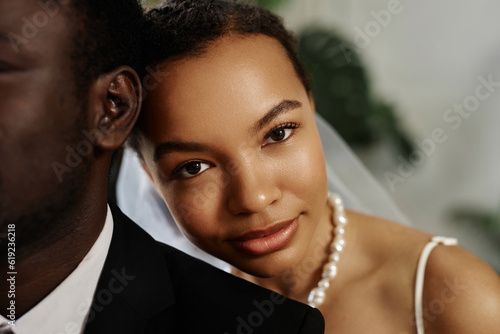 Closeup portrait of beautiful black woman as bride looking at camera over husbands shoulder