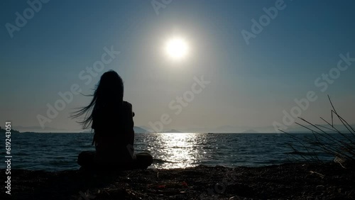 Silhouette of teen throw pebbles. A view of little girl throw small pebbles in the sea waves from the shore during nightfall in summer.