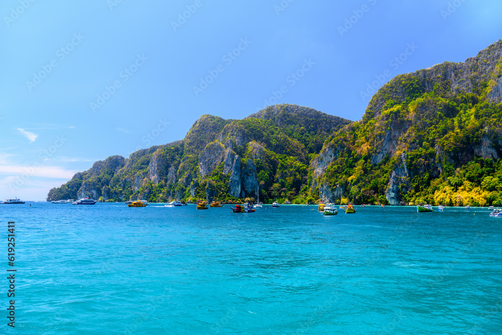 Fototapeta premium Boats and ships in the bay of Ko Phi Phi Don Island with huge rocks and cliffs on a sunny day, Ao Nang, Mueang Krabi District, Krabi, Andaman Sea, Thailand