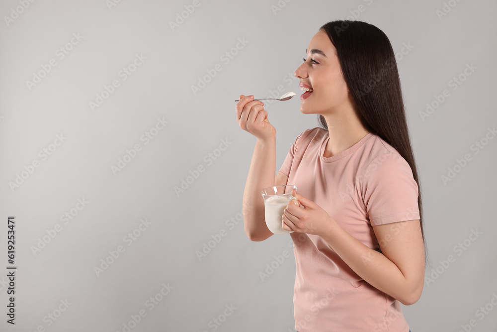 Happy woman eating tasty yogurt on grey background. Space for text Happy woman eating tasty yogurt on grey background. Space for text