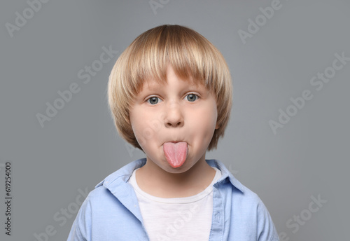 Cute little boy showing his tongue on grey background