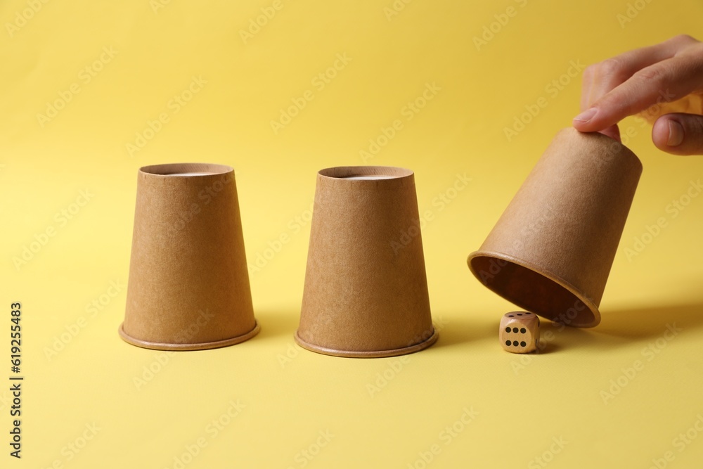 Woman showing dice under cup on yellow background, closeup. Thimblerig game Woman showing dice under cup on yellow background, closeup. Thimblerig game