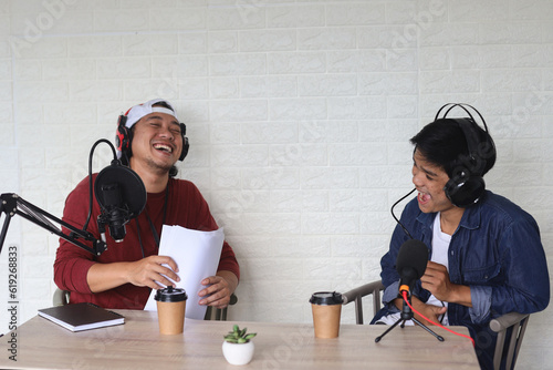 Male podcasters laughing happily while recording an audio broadcast in a studio. Two happy men recording an internet podcast for their social media channel. photo