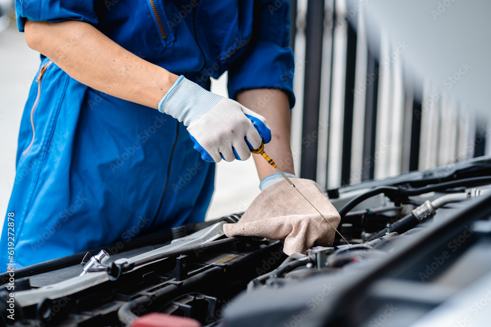 Obraz premium Close up, Auto mechanic repairman using tablet and pulling dipstick to checking engine oil level engine in the engine room, check the mileage of the car, oil change, auto maintenance service concept.
