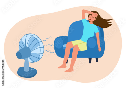 Woman sitting on sofa in front of an electric fan. She exhausted of hot summer day. Sweaty and thirsty.
