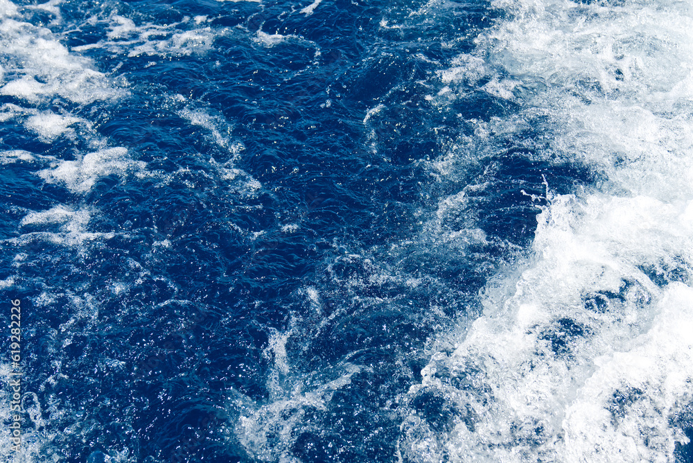 Abstract blue sea water with white waves. Blue sea texture with waves and foam. Rough deep turquoise and blue Mediterranean sea. Sea water top view.