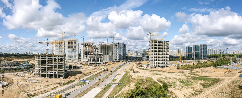 high-rise apartment buildings under construction and working cranes against blue cloudy sky. aerial panoramic view.