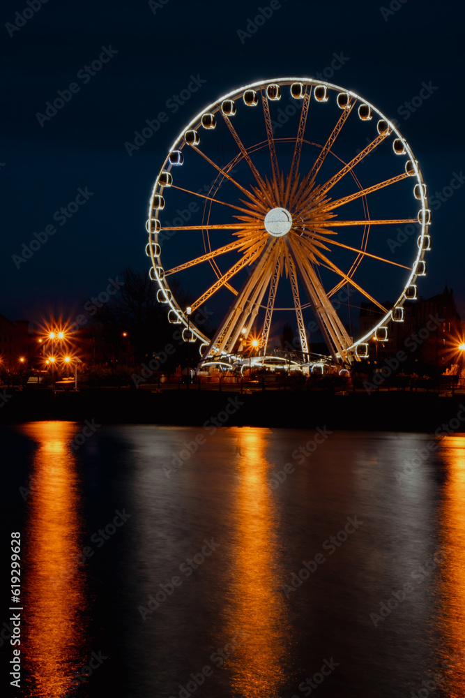 Gdansk Poland Ferris wheel in the old town of Gdansk at night evening dusk Reflection in river water Europe. Long exposure photo. City scenic view Illuminated attraction park and street with beautiful Gdansk Poland Ferris wheel in the old town of Gdansk at night evening dusk Reflection in river water Europe. Long exposure photo. City scenic view Illuminated attraction park and street with beautiful
