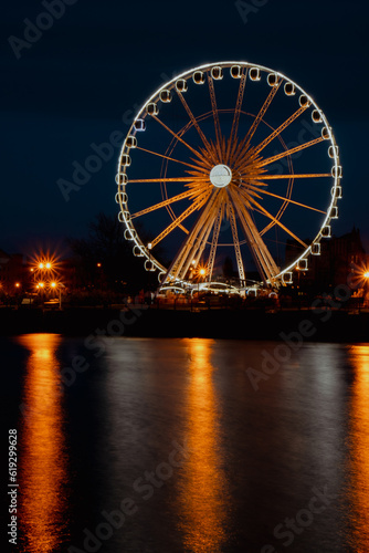 Gdansk Poland Ferris wheel in the old town of Gdansk at night evening dusk Reflection in river water Europe. Long exposure photo. City scenic view Illuminated attraction park and street with beautiful