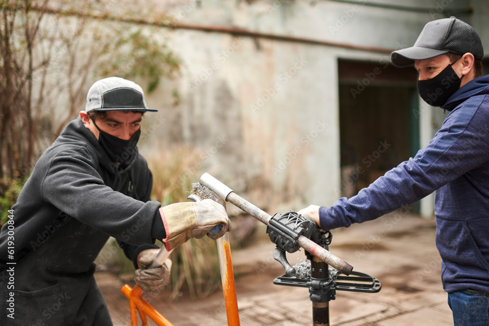 Young Hispanic men removing the paint of an orange bicycle frame, as part of a bike renovation work.