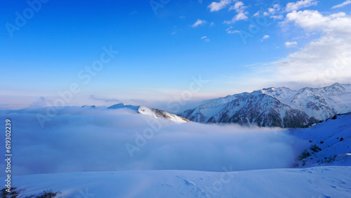 An ocean of clouds in the snowy mountains at dawn. White clouds are like a carpet in a gorge. Waves rise and descend from the mountains. Sunrise of the yellow sun. Clear sky  mountain peaks. Almaty