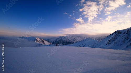 An ocean of clouds in the snowy mountains at dawn. White clouds are like a carpet in a gorge. Waves rise and descend from the mountains. Sunrise of the yellow sun. Clear sky, mountain peaks. Almaty © SergeyPanikhin