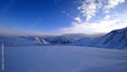 An ocean of clouds in the snowy mountains at dawn. White clouds are like a carpet in a gorge. Waves rise and descend from the mountains. Sunrise of the yellow sun. Clear sky  mountain peaks. Almaty
