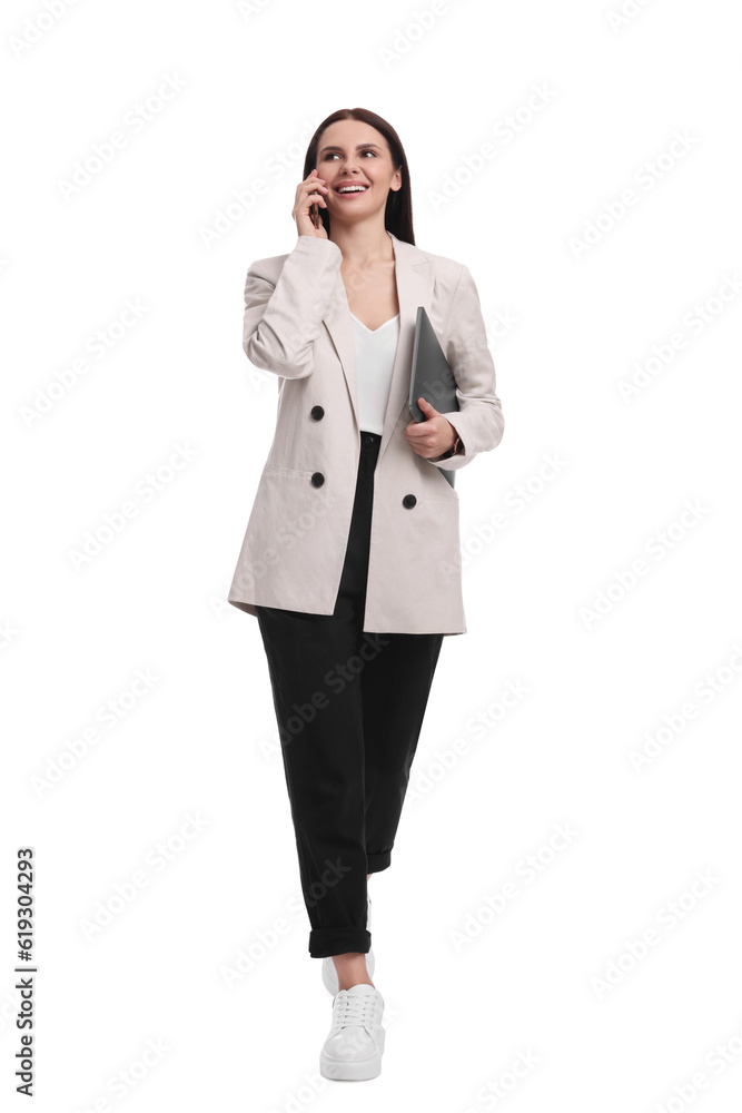 Beautiful businesswoman in suit with laptop talking on smartphone against white background Beautiful businesswoman in suit with laptop talking on smartphone against white background