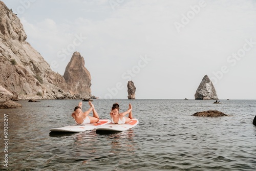 Woman sup yoga. Happy sporty woman practising yoga pilates on paddle sup surfboard. Female stretching doing workout on sea water. Modern individual female hipster outdoor summer sport activity. © panophotograph