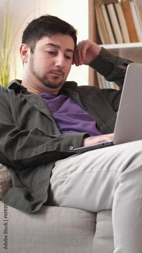 Vertical video. Remote work. Job fatigue. Gadget addiction. Tired overworked man freelancer workaholic typing at laptop napping on sofa at home. Vertical video. Remote work. Job fatigue. Gadget addiction. Tired overworked man freelancer workaholic typing at laptop napping on sofa at home.