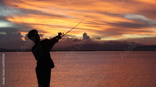 silhouette of a fisherman with a fishing rod in the lake at sunset