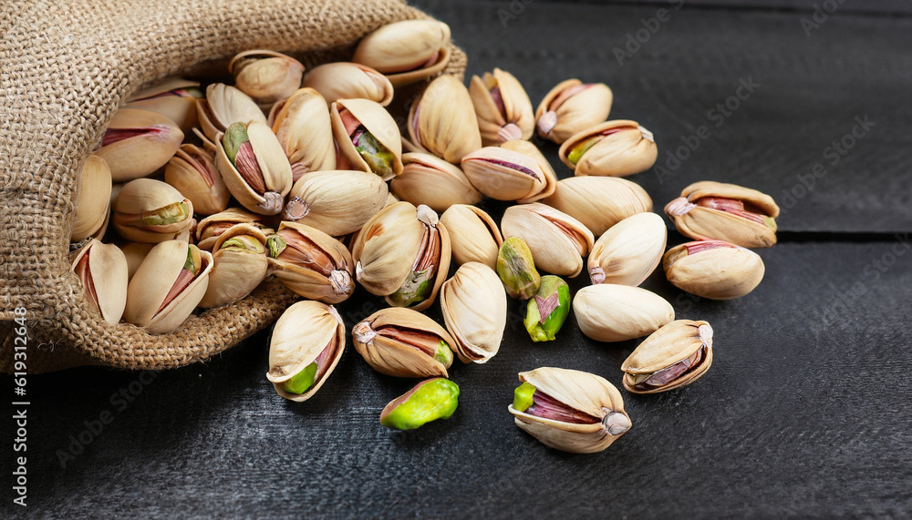 Pistachio in nutshell on black wooden rustic backdrop in burlap sack, composition of pistachios great for healthy and dietary nutrition. Concept of nuts