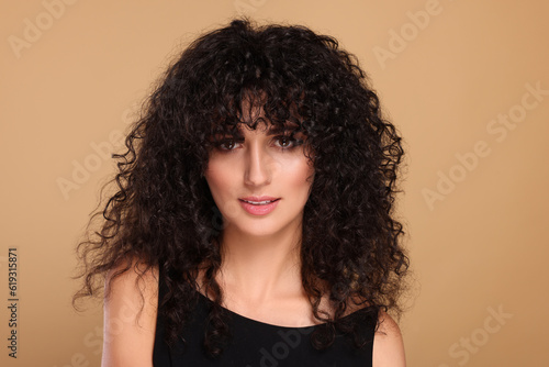 Beautiful young woman with long curly hair on beige background