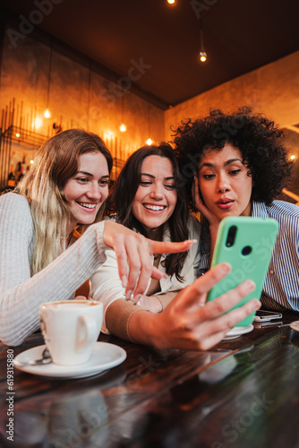 Vertical portrait of a group of young women having fun sharing media with an cellphone. Females looking the smartphone on a coffee shop. Girls shopping online on a marketplace using a mobile phone