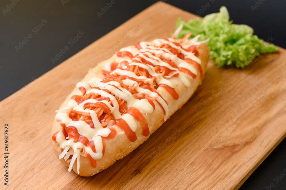 Hot dog covered with ketchup and mayonnaise on a wooden board on a black background. Hot dog covered with ketchup and mayonnaise on a wooden board on a black background.