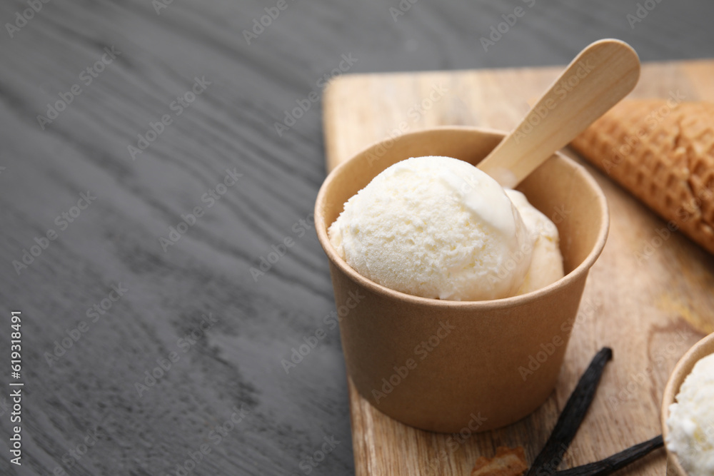 Paper cup with delicious ice cream and vanilla pods on grey wooden table, closeup. Space for text