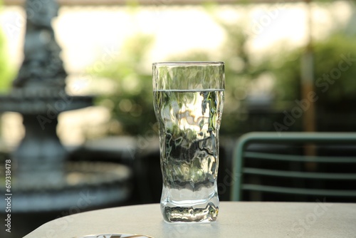 Glass of fresh water on light grey table outdoors