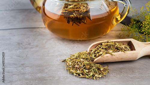 Herbal infusion fennel tea in glass cup and glass tea pot with dried fennel seeds in wooden shovel. Herbal tea alternative medicine background concept.