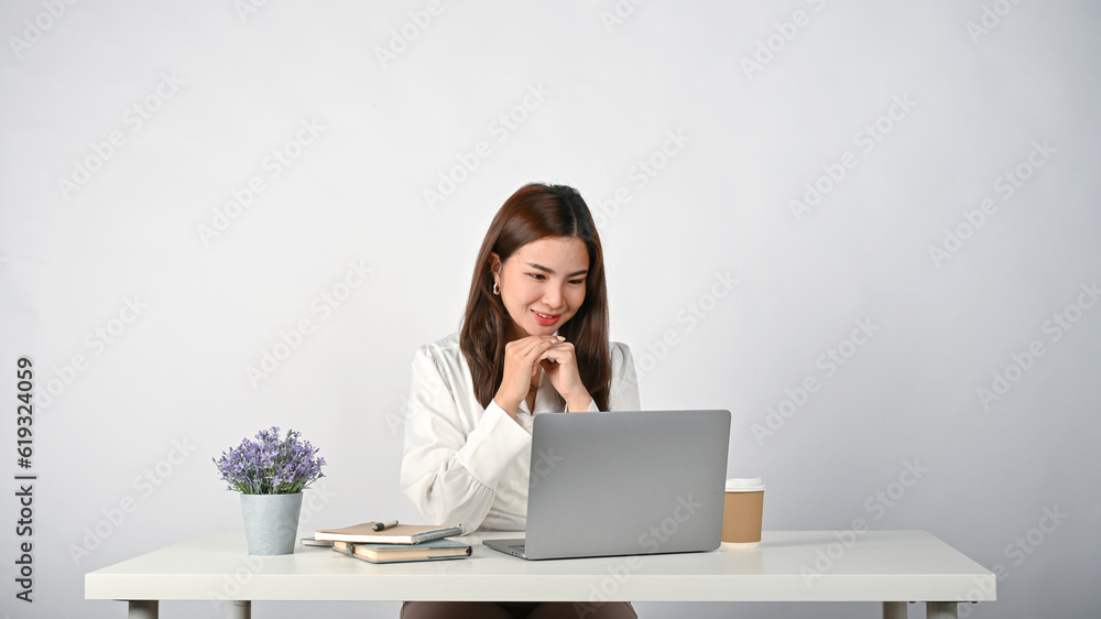 Office worker is putting her hands together and looking down at her laptop screen with happiness Office worker is putting her hands together and looking down at her laptop screen with happiness
