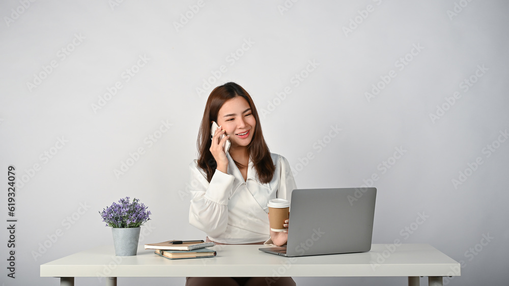 A beautiful Asian businesswoman is on the phone with a client while sitting at her desk. A beautiful Asian businesswoman is on the phone with a client while sitting at her desk.