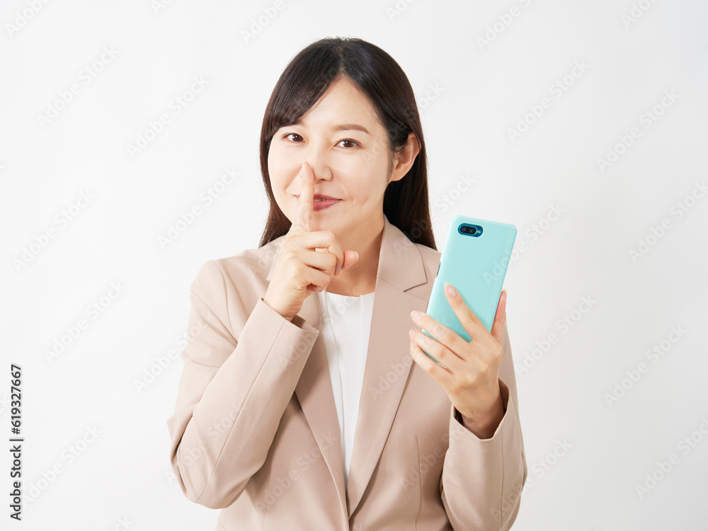 スマートフォンを持って内緒のポーズをするミドルエイジのビジネスウーマン 白背景 スマートフォンを持って内緒のポーズをするミドルエイジのビジネスウーマン 白背景