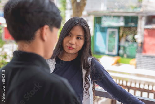A lovely young lady in a white cardigan and long sleeves blue navy top and has a serious look, is conversing with a guy in a black polo shirt. A house is shown in the background.