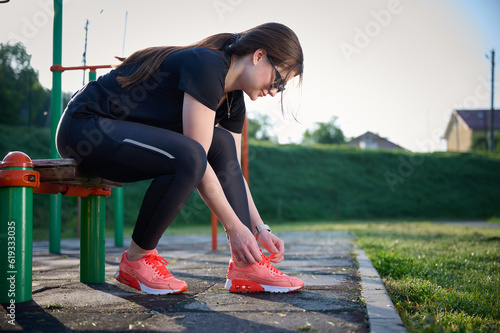 ?lose up view of a girl tying shoelaces, sporty female wearing sneakers at the tartan track and walking. Sporty female sitting near the stadium on the jogging track. photo