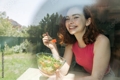 Happy young woman with salad bowl seen through glass photo