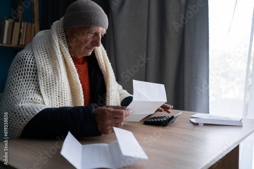 Senior man opening UK energy bill concerned about cost of living energy crisis, old male in cold home photo