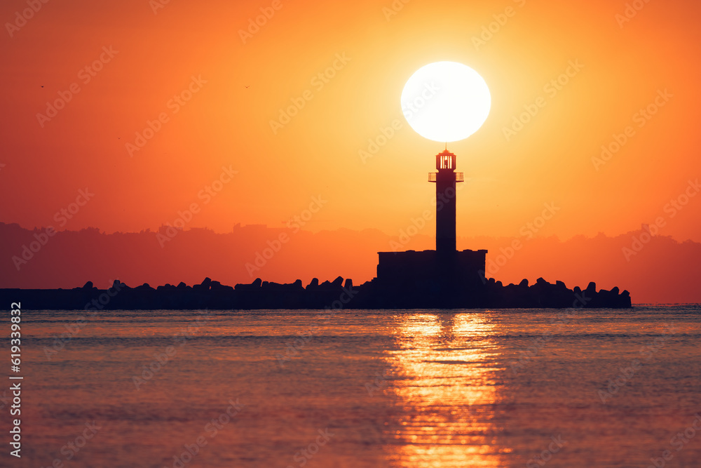 Seascape of sunrise over sea lighthouse and coastal beach shore