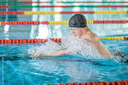 Male athlete swimming in breaststroke style in the pool, stroke, immerse, and lift out of the water to breathe.