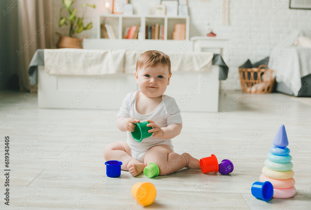 baby 6-9 months old playing with a colorful rainbow toy pyramid sitting in a white sunny bedroom. Toys for small children. Children's interior. A child with an educational toy. baby 6-9 months old playing with a colorful rainbow toy pyramid sitting in a white sunny bedroom. Toys for small children. Children's interior. A child with an educational toy.