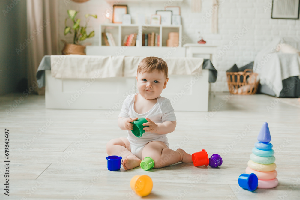 baby 6-9 months old playing with a colorful rainbow toy pyramid sitting in a white sunny bedroom. Toys for small children. Children's interior. A child with an educational toy. baby 6-9 months old playing with a colorful rainbow toy pyramid sitting in a white sunny bedroom. Toys for small children. Children's interior. A child with an educational toy.