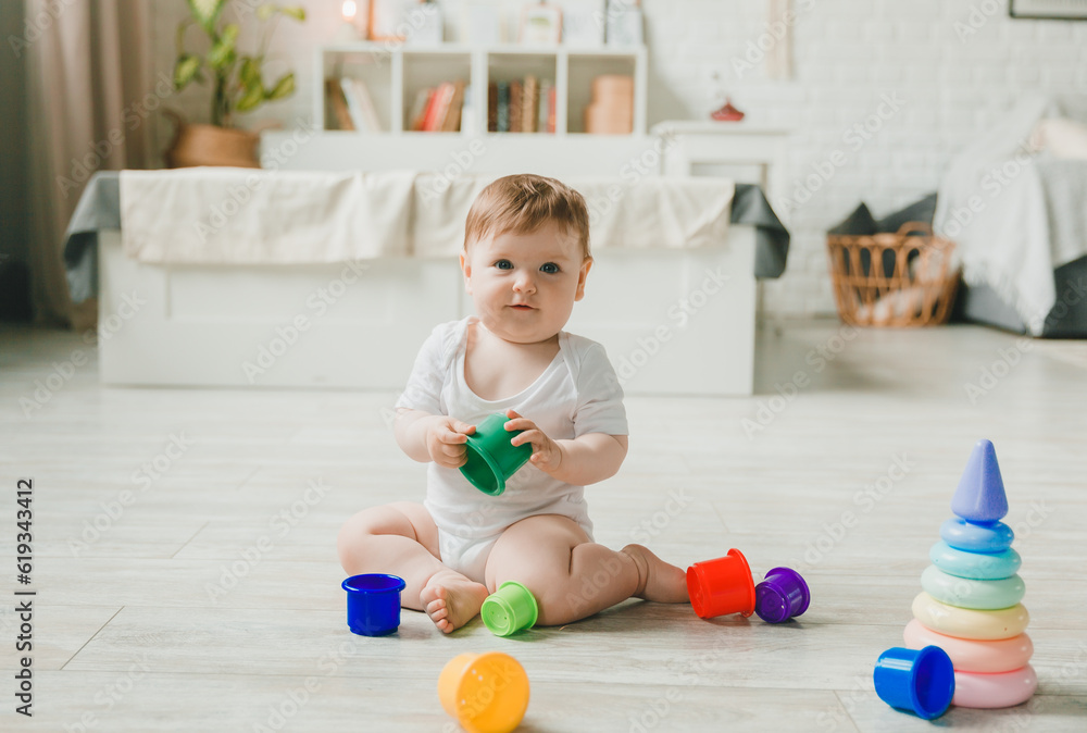 baby 6-9 months old playing with a colorful rainbow toy pyramid sitting in a white sunny bedroom. Toys for small children. Children's interior. A child with an educational toy. baby 6-9 months old playing with a colorful rainbow toy pyramid sitting in a white sunny bedroom. Toys for small children. Children's interior. A child with an educational toy.