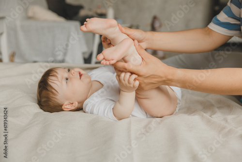 Mom makes a foot massage for a 6-month-old baby at home on the bed. mother plays with the baby at home.