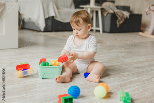baby 6-9 months old playing with a colorful rainbow toy pyramid sitting in a white sunny bedroom. Toys for small children. Children's interior. A child with an educational toy. © inna717