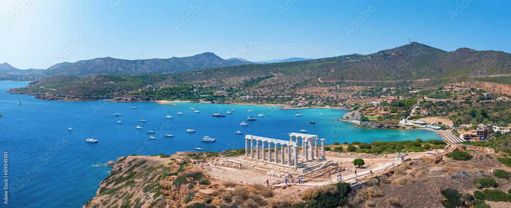 Fototapeta premium Panoramic view of the Temple of Poseidon at Cape Sounion at the edge of Attica, Greece, with moored sailboats in the bay during summer time