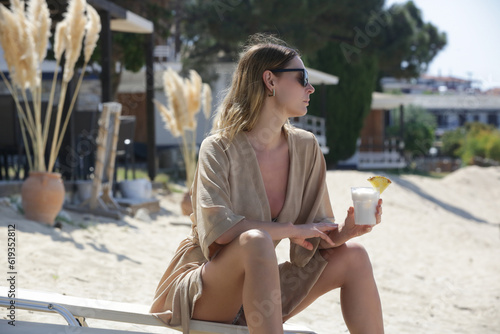 Tourist woman in linen robe havin cocktail in a beach bar, relaxed solo vacation concept