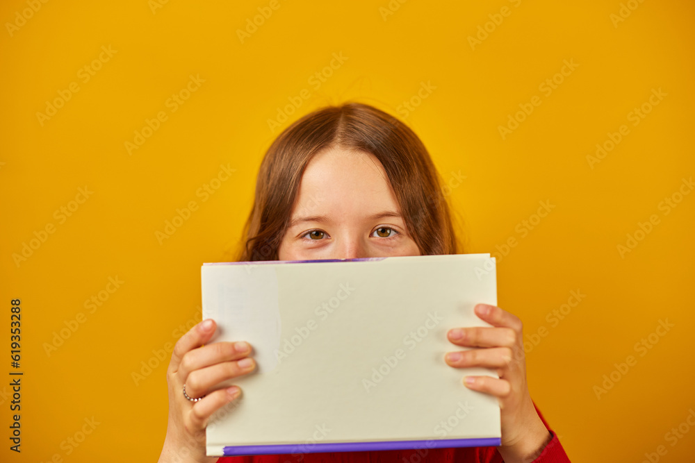 Portrait of happy teenage schoolgirl cover her face by book Portrait of happy teenage schoolgirl cover her face by book