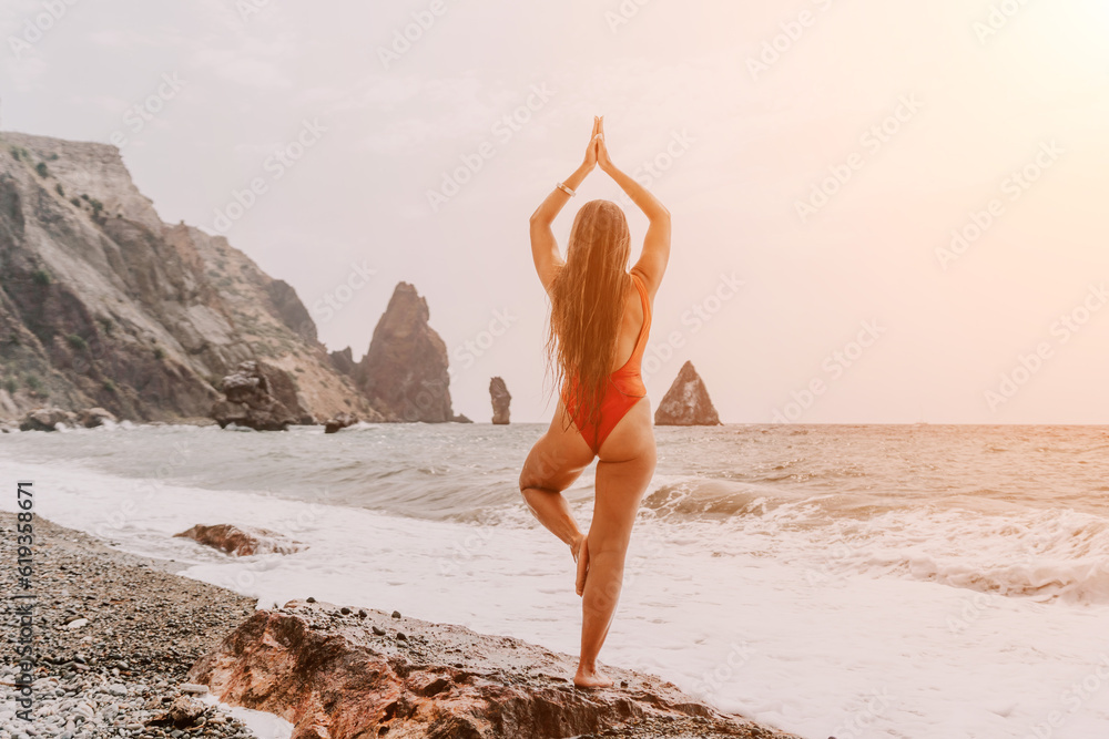 Woman sea yoga. Back view of free calm happy satisfied woman with long hair standing on top rock with yoga position against of sky by the sea. Healthy lifestyle outdoors in nature, fitness concept. Woman sea yoga. Back view of free calm happy satisfied woman with long hair standing on top rock with yoga position against of sky by the sea. Healthy lifestyle outdoors in nature, fitness concept.