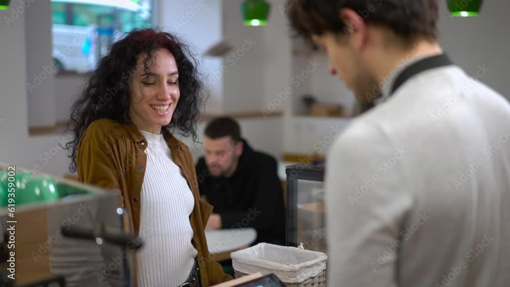 Positive young woman smiling talking with man ordering coffee in cafe. Charming Caucasian female client and male barista in the morning in urban city Positive young woman smiling talking with man ordering coffee in cafe. Charming Caucasian female client and male barista in the morning in urban city