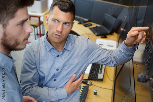 manager interrogating younger worker while pointing to computer monitor