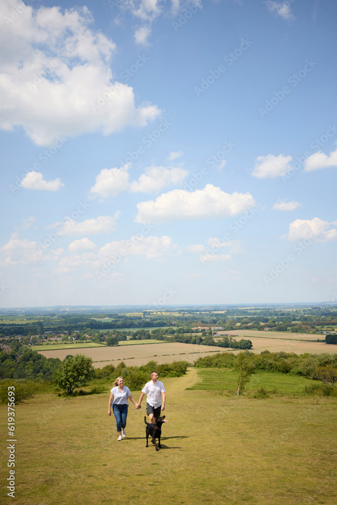 Loving Mature Couple Walking With Pet Dog Through Beautiful English Countryside In Oxfordshire England UK