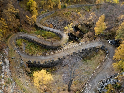 Aerial view of people walking down a curvy path in a forest in autumn © Kjell Værøy Ljøstad/Wirestock Creators